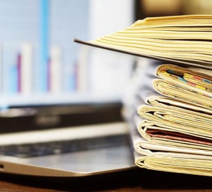 Stack of folders and documents beside an open laptop, with a blurred chart on the screen in the background.